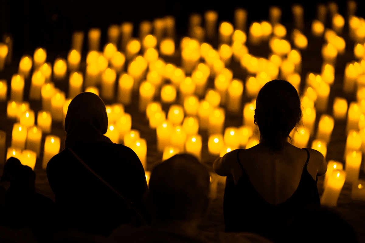 The silhouette of an audience looking out across a sea of candles.