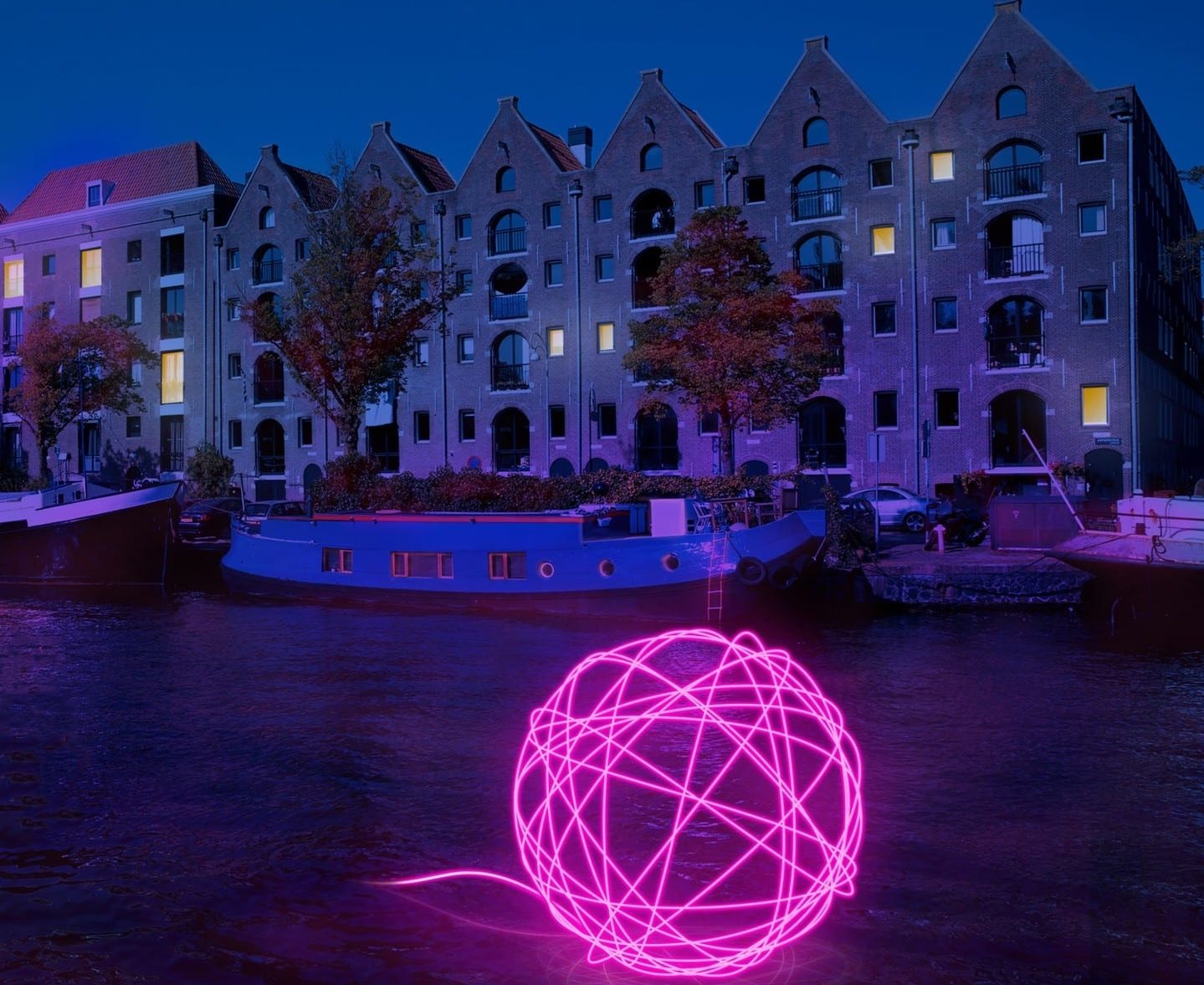 A bright pink, illuminated ball of strong sits afloat a canal at Amsterdam Light Festival.