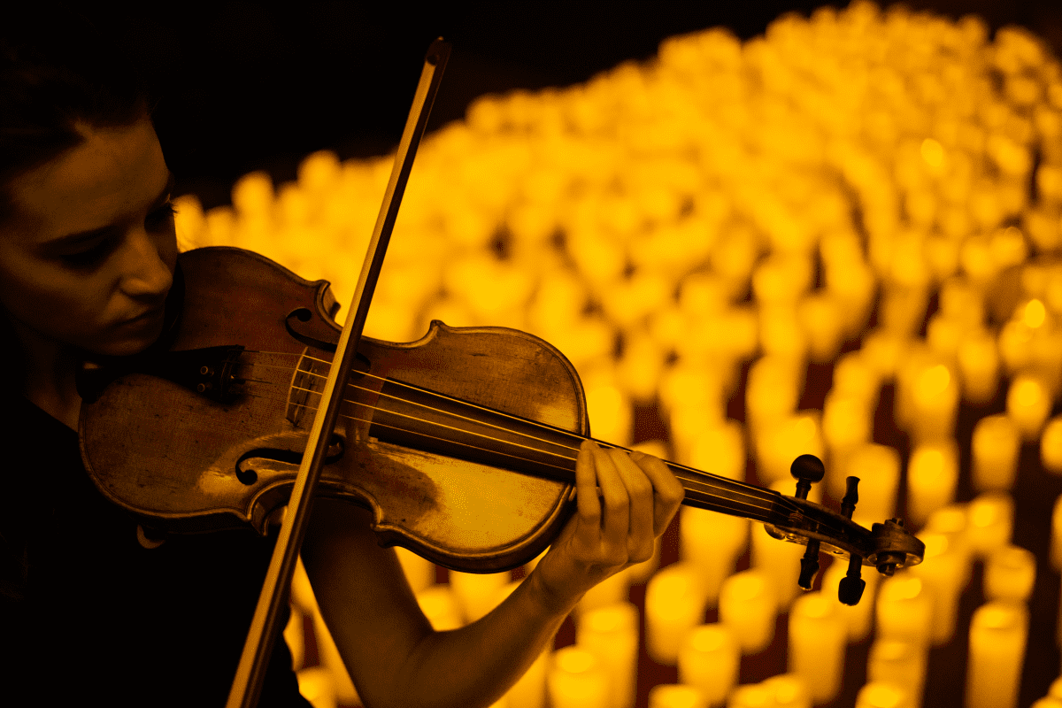 A close up of a woman playing the violin with a sea of candles behind her.