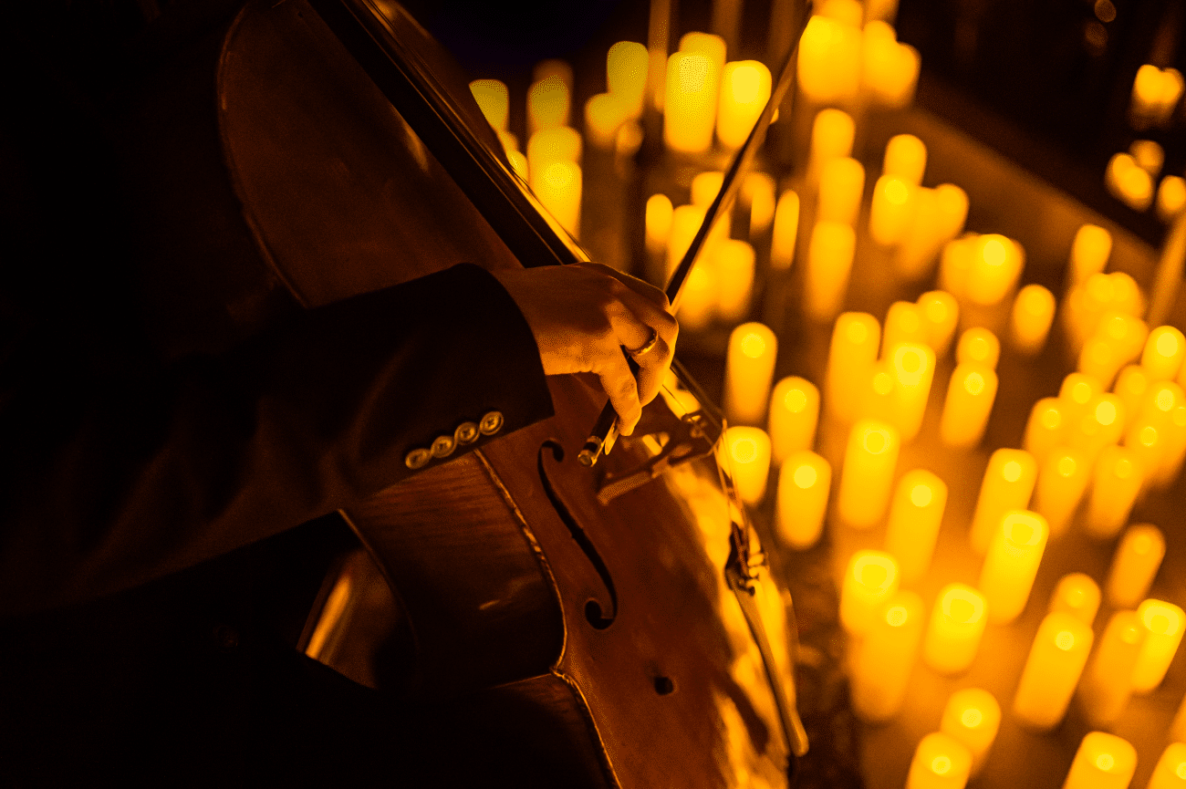 A close up of a hand playing a cello with candles around it.
