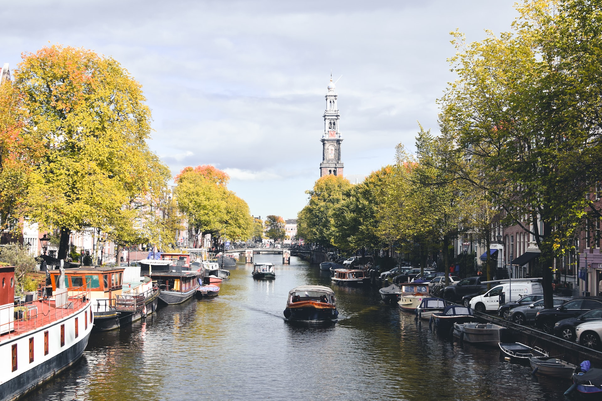 A boat saild down a canal in Amsterdam, which is lined with boats, in warm weather.