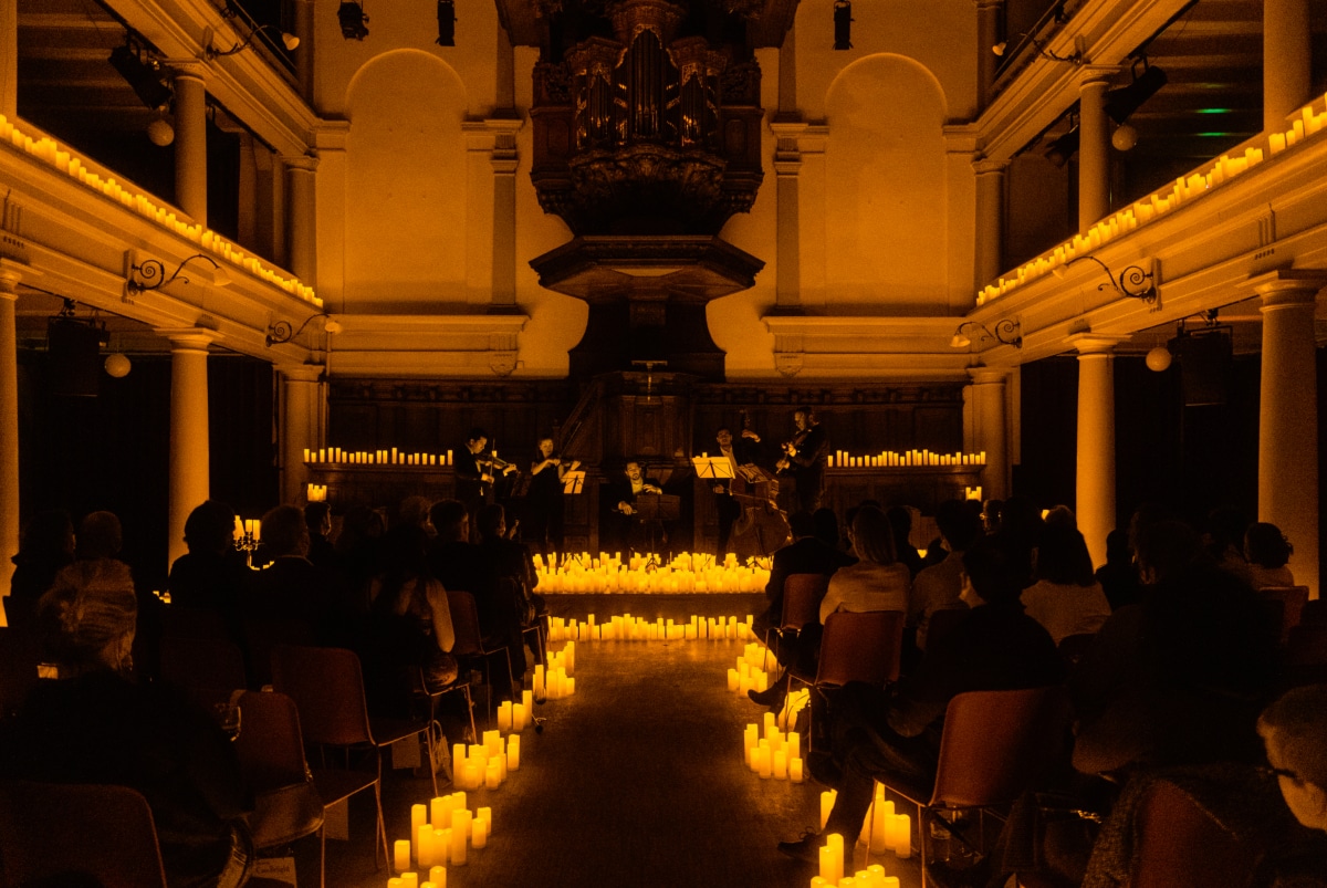 A string quartet performing at Rode Hoed surrounded by candles while an audience watches.