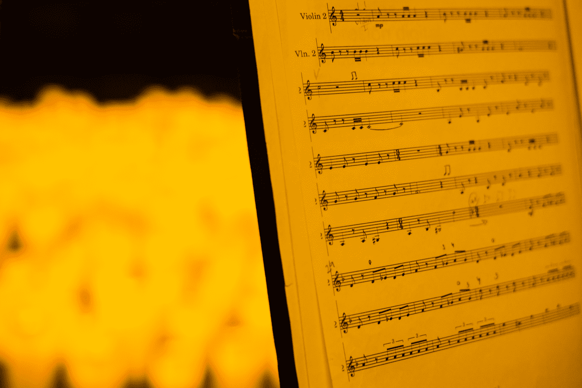 A close up a music sheet on a stand with the blurry glow of candles behind it.