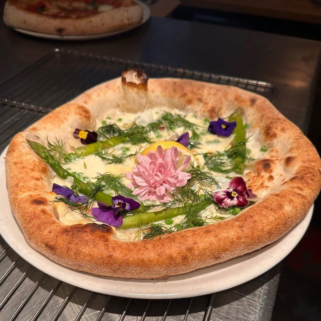 A pizza topped with white sauce, flowers and asparagus at Lou Lou Pizza Bar. 