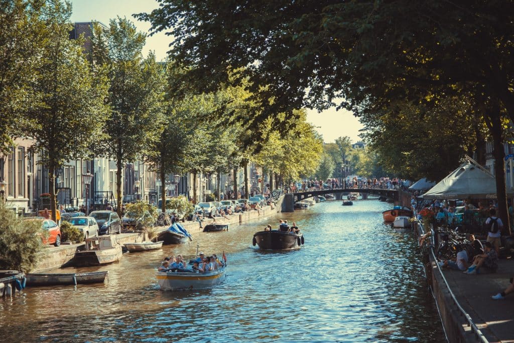 One of Amsterdam's canals, surrounded by trees, where boats are sailing.