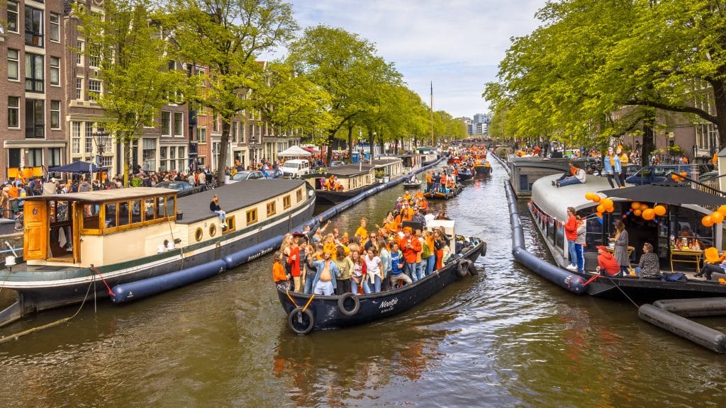 Boats on a canal in Amsterdam carry people celebrating King's Day.