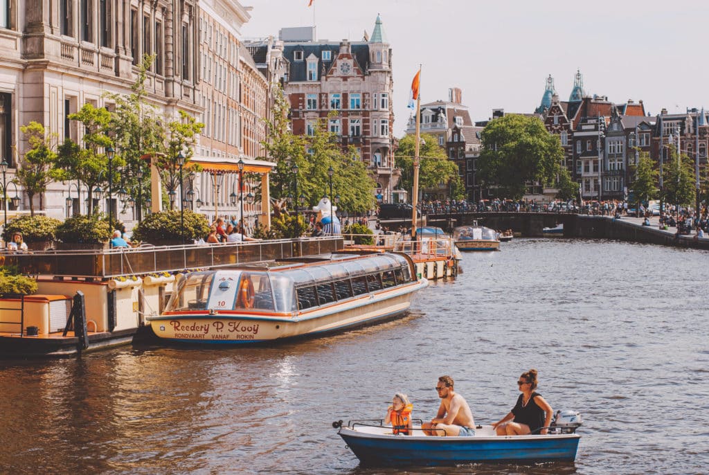 People sit on boats on a canal in Amsterdam.