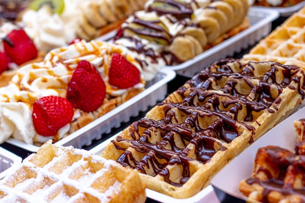 Trays of waffles topped with strawberries and chocolate.